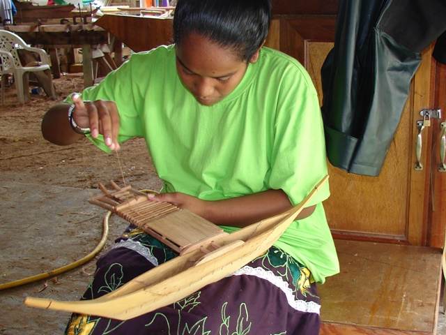 A trainee lashes the platform between the outrigger and the hull on a model canoe.