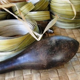 One of the heavy pounders known as dekã in nin that are used to soften the dried pandanus leaves, shown in coils behind the pounder.