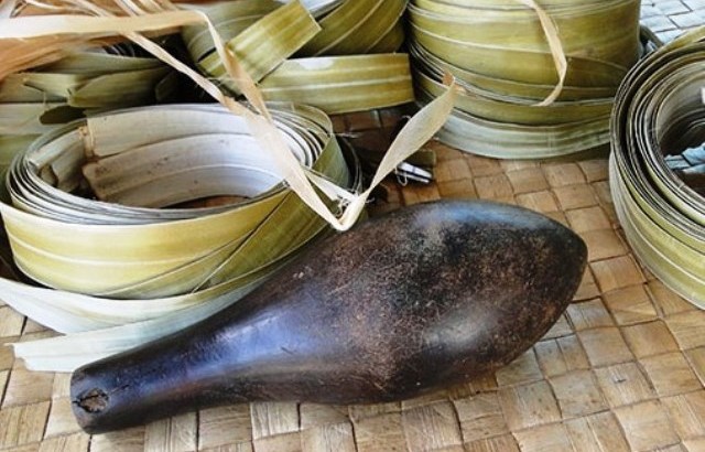 One of the heavy pounders known as dekã in nin that are used to soften the dried pandanus leaves, shown in coils behind the pounder.