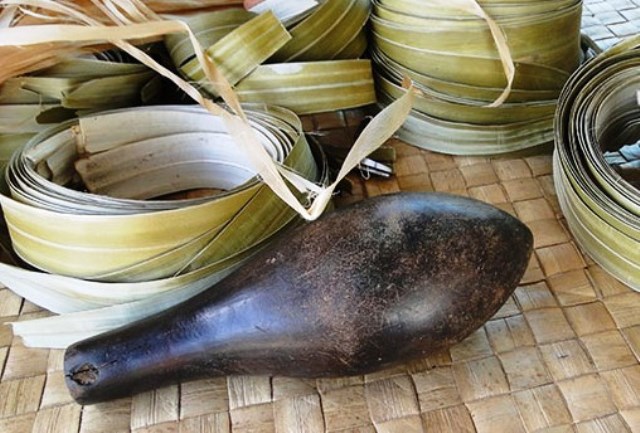 One of the heavy pounders known as dekã in nin that are used to soften the dried pandanus leaves, shown in coils behind the pounder.